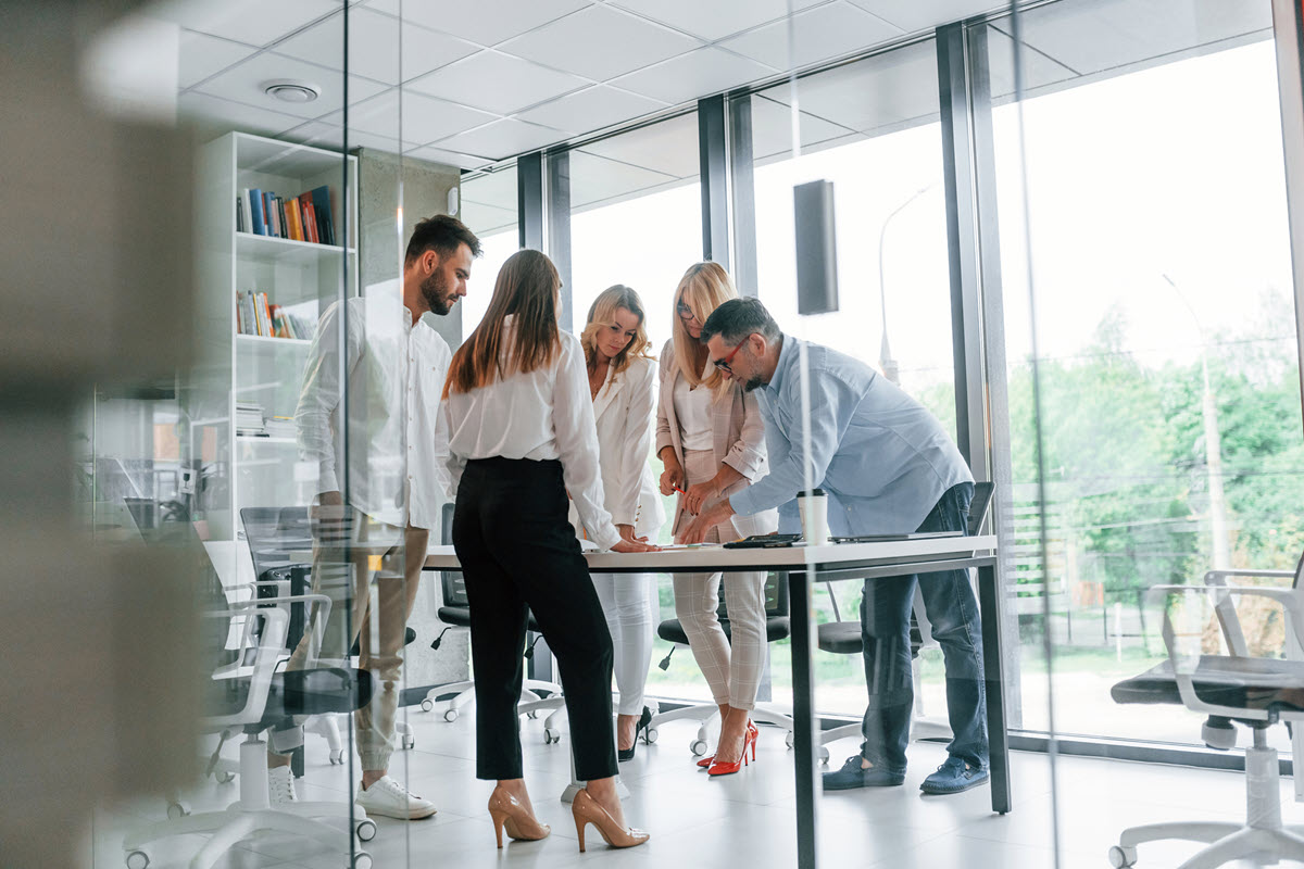 Group of professional business people collaborating near big windows in an office, symbolizing the importance of teamwork and success in implementing Six Sigma.