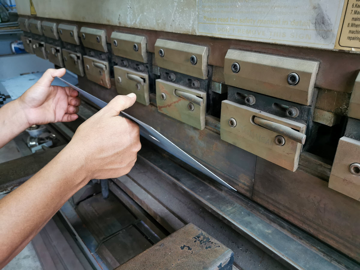 A worker precisely cutting a metal plate with a specialized machine as part of a process capability analysis example.