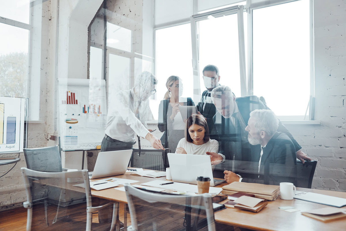 Business team in a board room, working collaboratively and using modern technologies, embodying the concept of a soft-wired organization within the Six Sigma management paradox.