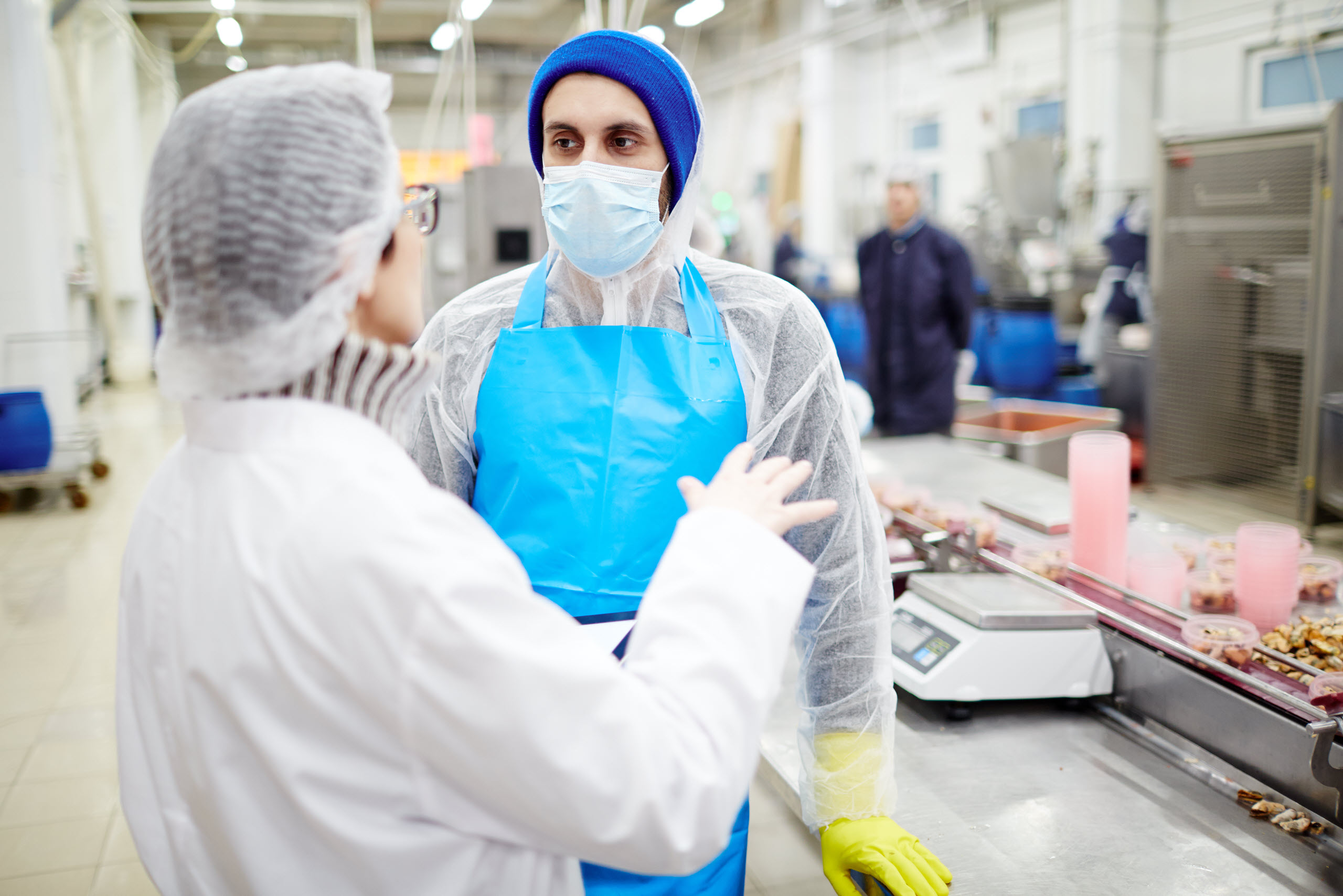 Man and woman engaged in a discussion about food quality in a food processing plant, representing the "Cost Reduction Strategies for Food Processing" course, focused on optimizing processes and reducing costs while upholding food safety and quality standards.