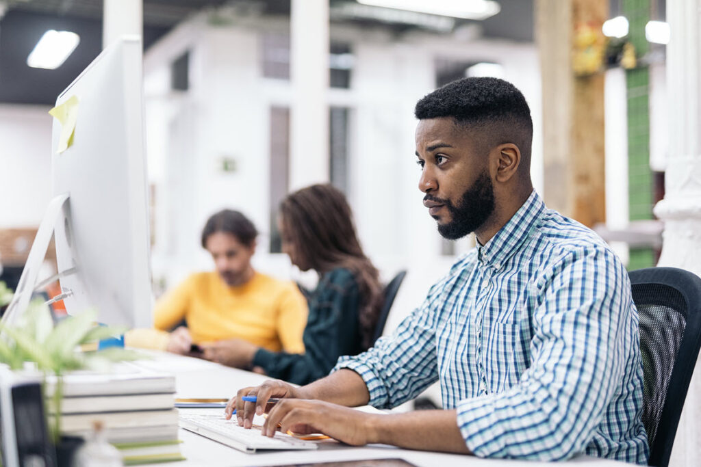 Focused African American man engaged in Lean Overview Training on his desktop computer, likely learning about the basic principles and tools of Lean methodology to improve processes in his organization.