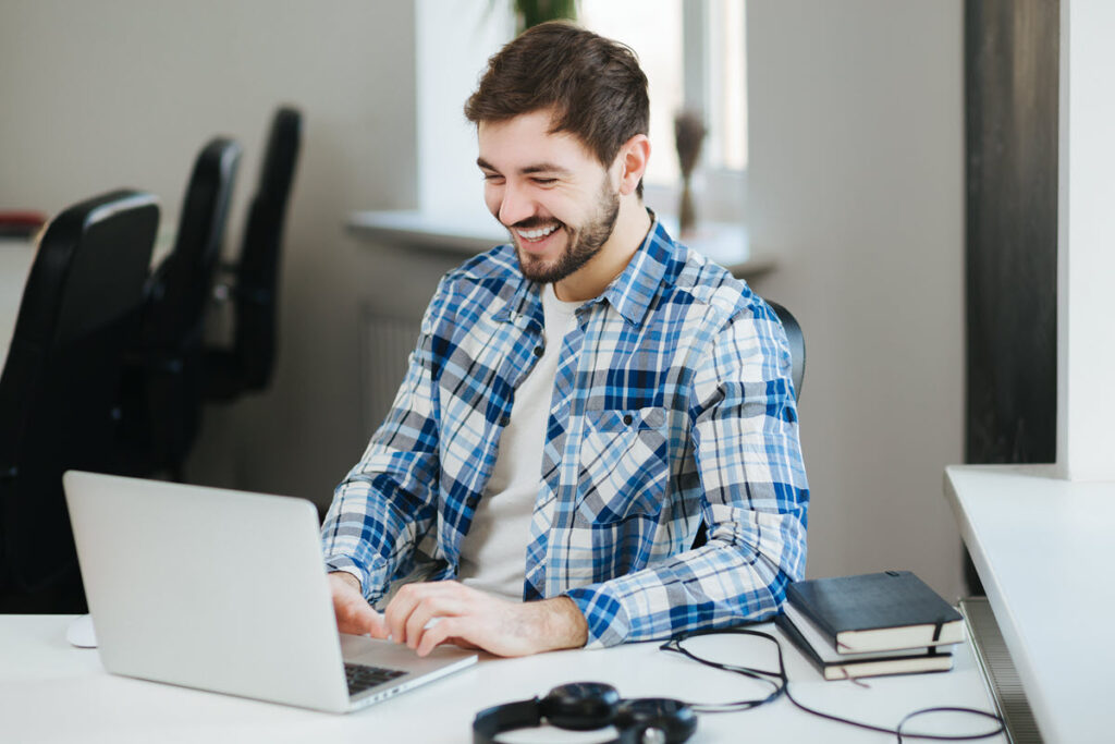 Smiling man engaged in Lean Overview Training on his laptop in conference room, likely learning about basic principles and tools of Lean methodology, such as process mapping, waste reduction, and continuous improvement.