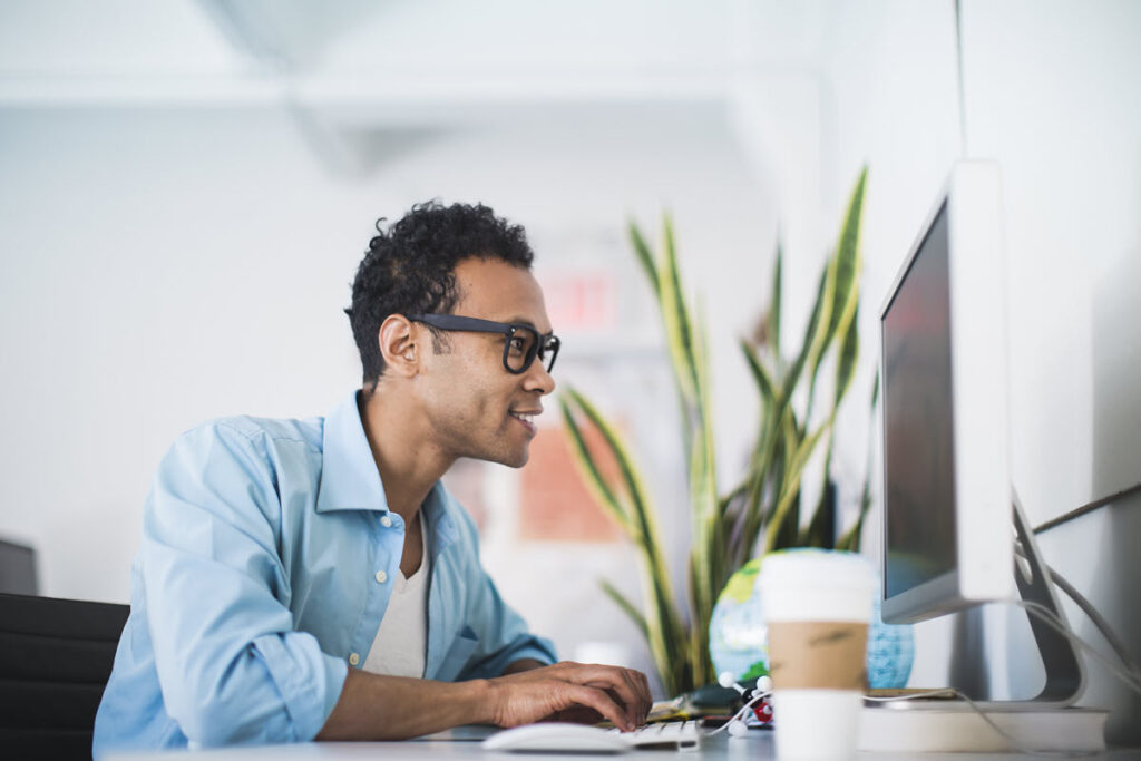 Man wearing glasses working on Lean Six Sigma Yellow Belt Training on his computer, using data analysis, process mapping, or statistical tools to improve processes.