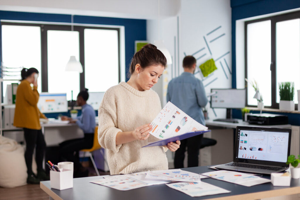 Woman reviewing printed graphs and charts for Lean Six Sigma Yellow Belt Training, standing next to her computer, analyzing data to improve processes.